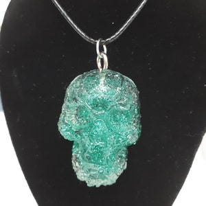 May include: A green glass skull pendant on a black leather cord necklace.