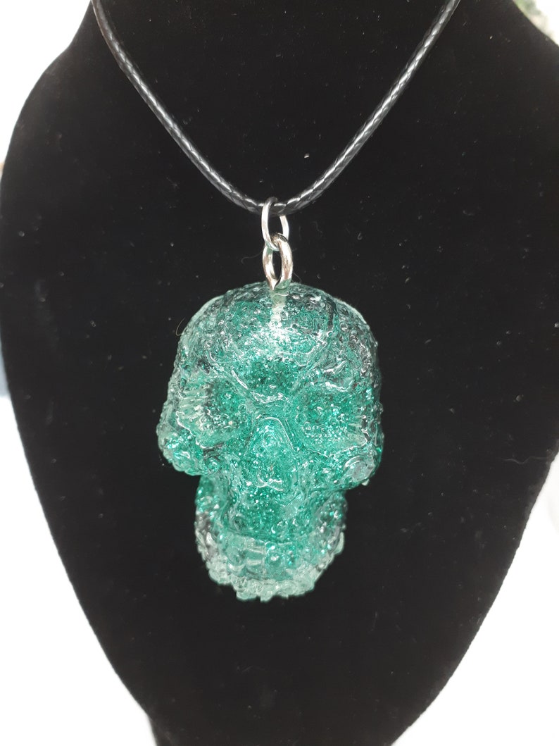 May include: A green glass skull pendant on a black leather cord necklace.