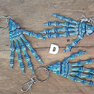 May include: Three skeleton hand keyrings with silver key rings. The hands are painted in a blue and silver iridescent colour.