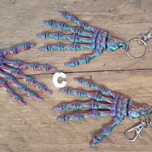 May include: Two iridescent skeleton hand keyrings with silver key rings and clasps. The hands are a mix of blue, green, and purple.