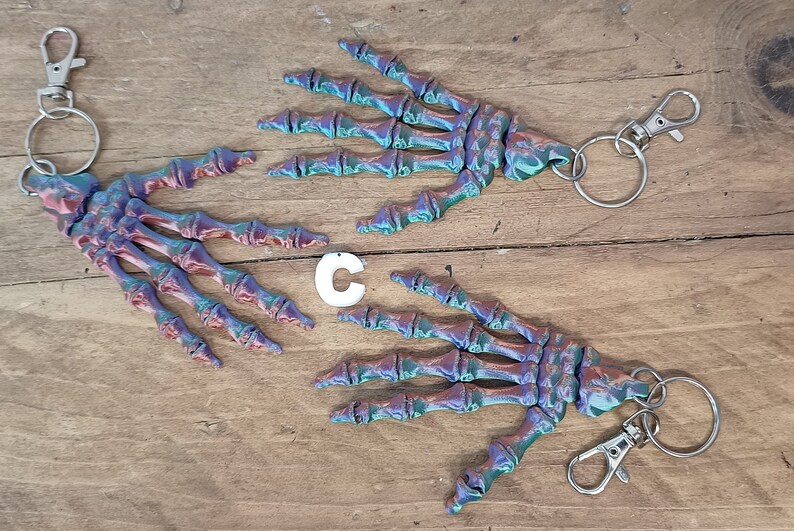May include: Two iridescent skeleton hand keyrings with silver key rings and clasps. The hands are a mix of blue, green, and purple.