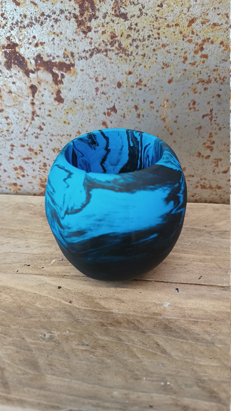 May include: A small, round planter made of blue and black marbled resin. The planter has a smooth, glossy finish.