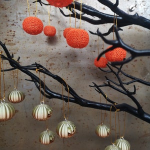 K&ouml;nnte beinhalten: Ein schwarzer Ast mit orangefarbenen und gr&uuml;nen Ornamenten, die daran h&auml;ngen. Die Ornamente sind rund und haben eine strukturierte Oberfl&auml;che.