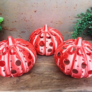 May include: Three red and white pumpkin-shaped candle holders with a cut-out design.