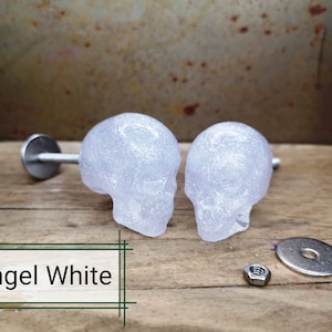 Peut inclure: Deux poignées de tiroir en forme de crâne blanches avec une finition scintillante. Les poignées sont présentées avec les vis et les rondelles nécessaires à l'installation. Le texte "Angel White" est visible sur l'image.