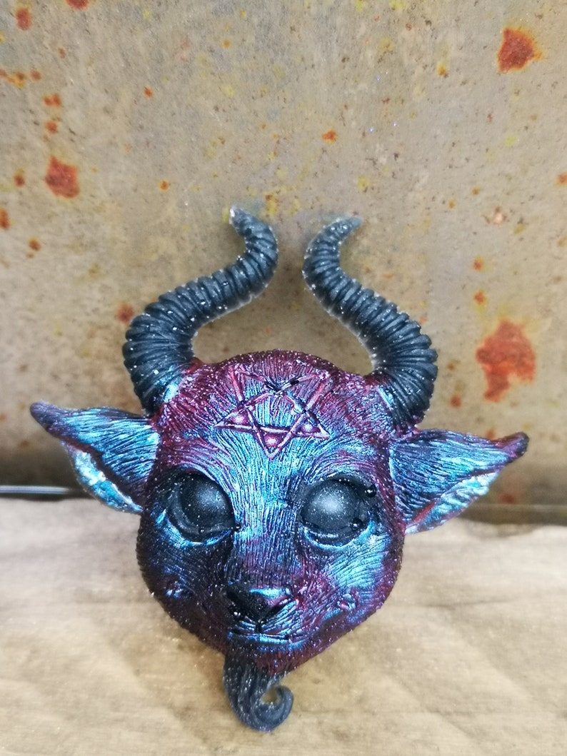 Puede incluir: Una peque&ntilde;a escultura de resina azul y roja de un demonio con cuernos y un pentagrama en la frente.