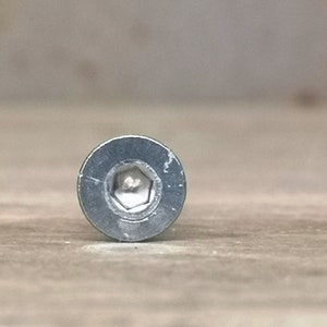 May include: Close-up of the head of a silver screw with a hexagonal head.