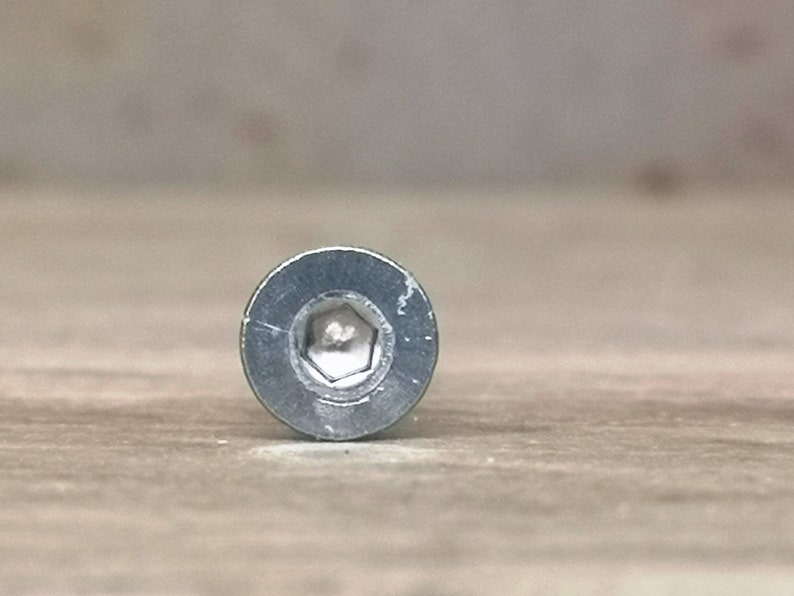 May include: Close-up of the head of a silver screw with a hexagonal head.