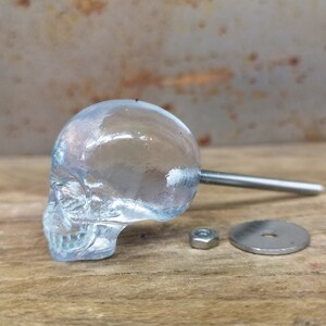 May include: A clear glass skull door knob with a silver metal screw and washer.
