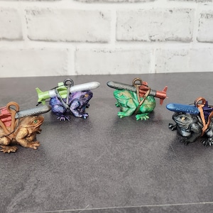 May include: Four frog figurines, each carrying a different colored missile on their backs. The frogs are painted in various colors, including green, purple, brown, and black.
