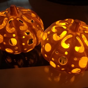 May include: Two white, intricately carved pumpkin-shaped lanterns with a warm, glowing light emanating from the inside.
