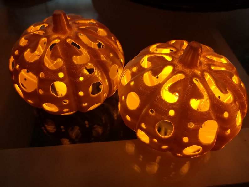 May include: Two white, intricately carved pumpkin-shaped lanterns with a warm, glowing light emanating from the inside.