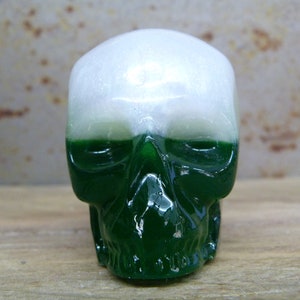May include: A white and green skull made of resin. The top of the skull is white and the bottom is green.