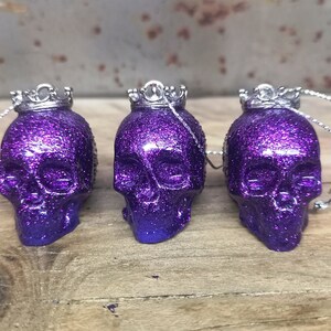May include: Three purple glitter skull ornaments with silver crowns and silver strings.