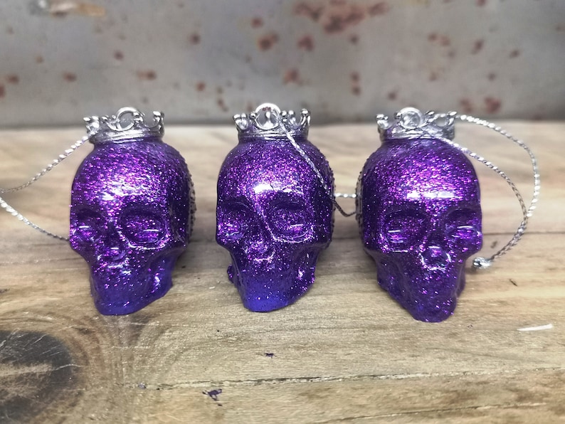 May include: Three purple glitter skull ornaments with silver crowns and silver strings.