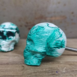 May include: A green and white skull-shaped cabinet knob with a metal screw. The skull has a marbled pattern with green swirls.