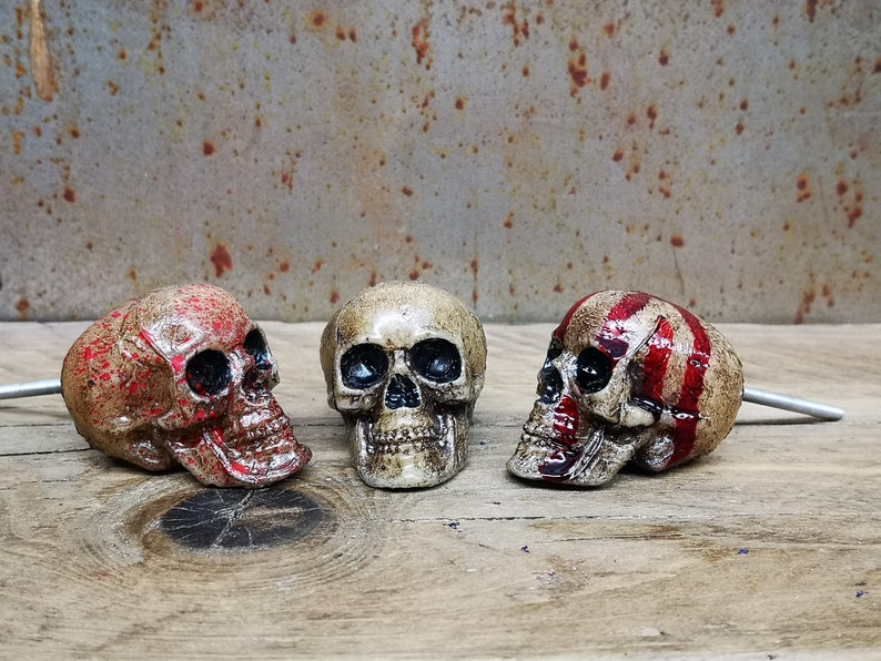 May include: Three decorative skull drawer pulls with a distressed finish. The skulls are painted in shades of red and white. The pulls are made of metal and have a screw on the back.