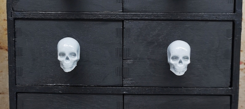 May include: Black dresser with white ceramic skull drawer pulls.
