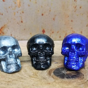 May include: Three small skull figurines, one silver, one black, and one blue.