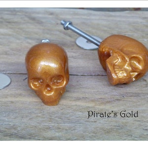May include: Two gold skull-shaped cabinet knobs with silver screws. The text "Pirate's Gold" is visible below the knobs.