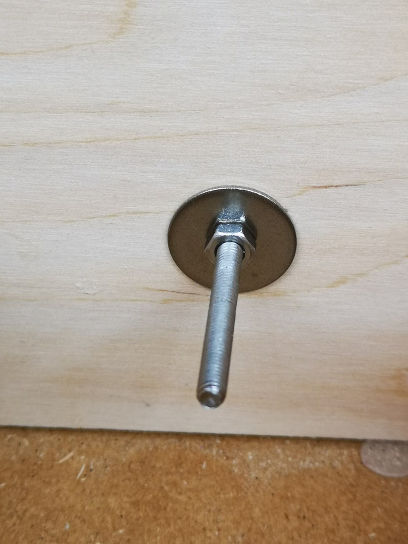 May include: A silver metal bolt with a washer and nut attached to a piece of wood.