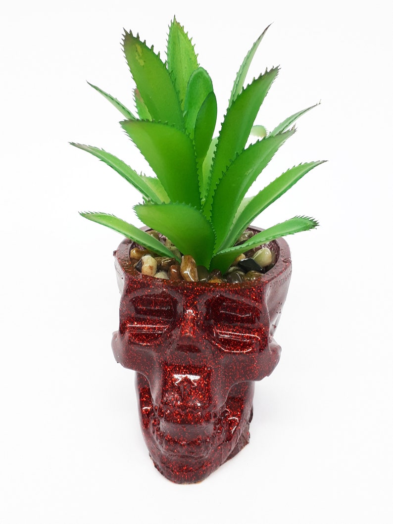 Pode incluir: Um vaso de caveira vermelho com glitter com uma planta suculenta verde dentro. O vaso &eacute; feito de cer&acirc;mica e tem um acabamento brilhante.