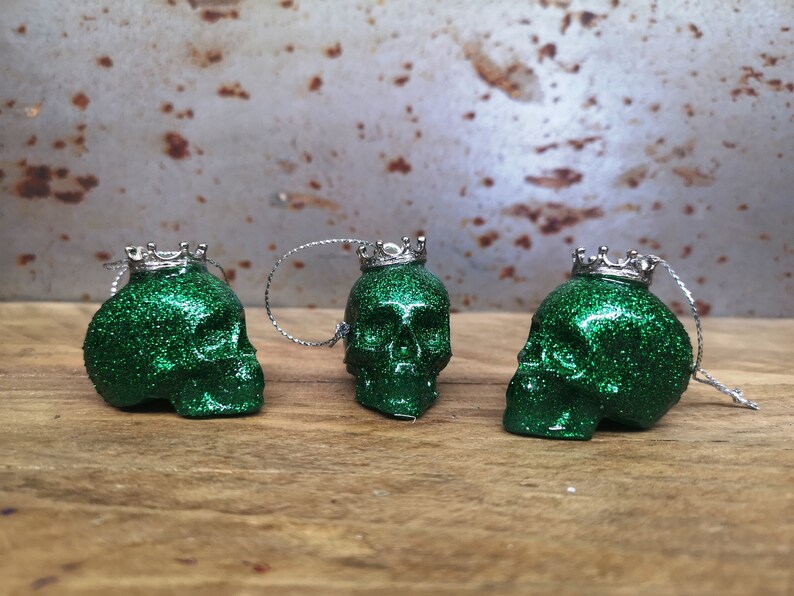 May include: Three green glitter skull ornaments with silver crowns. Each skull has a silver loop for hanging.