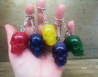 May include: Five colorful skull keychains in red, blue, yellow, purple, and green. Each skull is attached to a silver chain and keyring. The keychains are made of a translucent material.