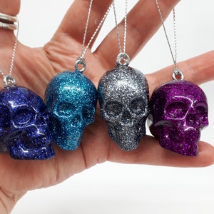 May include: Four glitter skull ornaments in blue, teal, silver, and purple. Each skull is hanging from a silver string.
