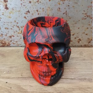 May include: A red and black skull-shaped planter with a marbled design.