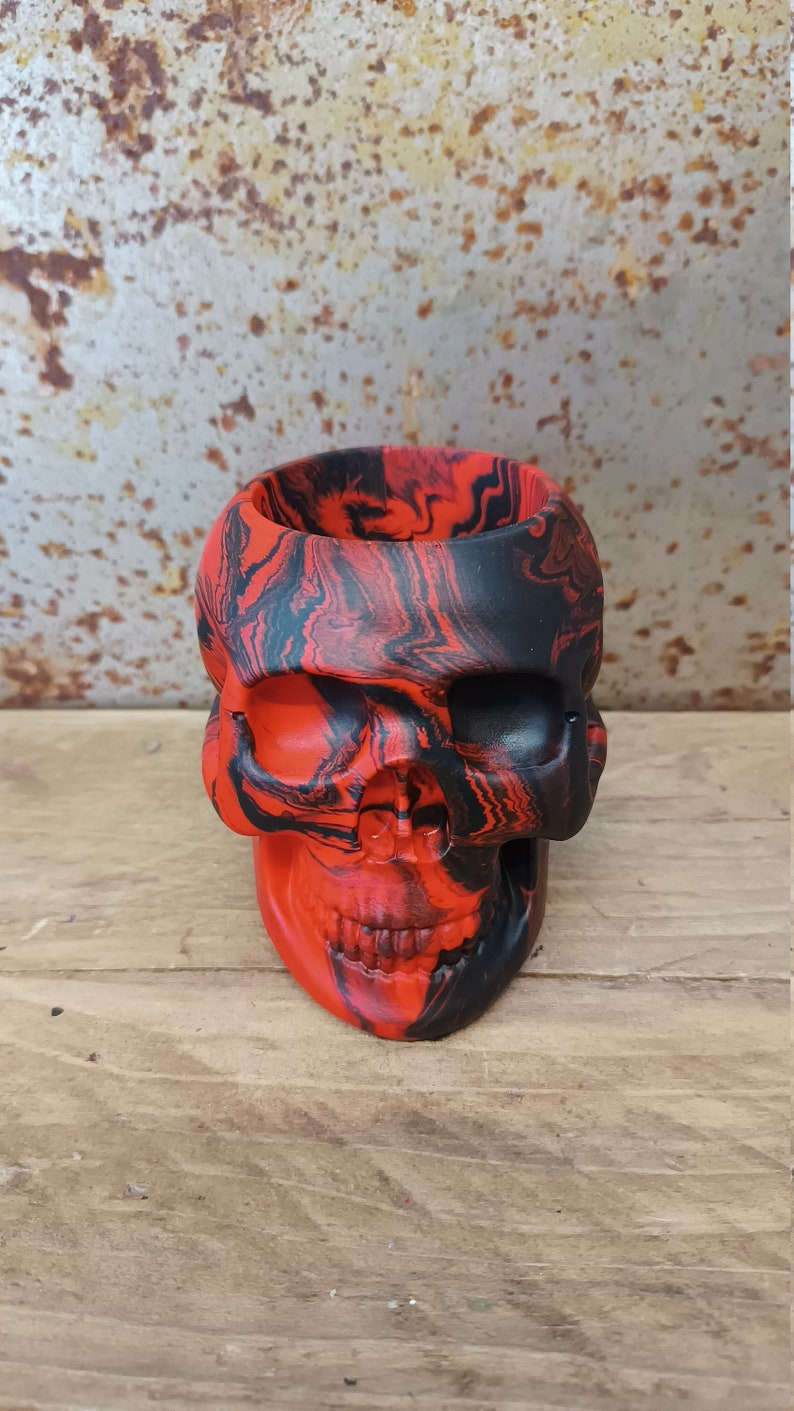 May include: A red and black skull-shaped planter with a marbled design.