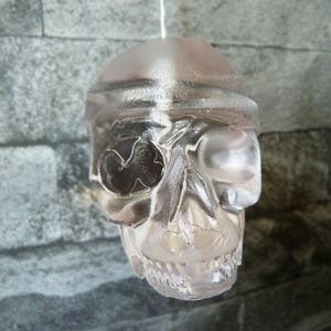 May include: A clear glass skull ornament with a pirate eye patch. The skull is hanging from a white string.