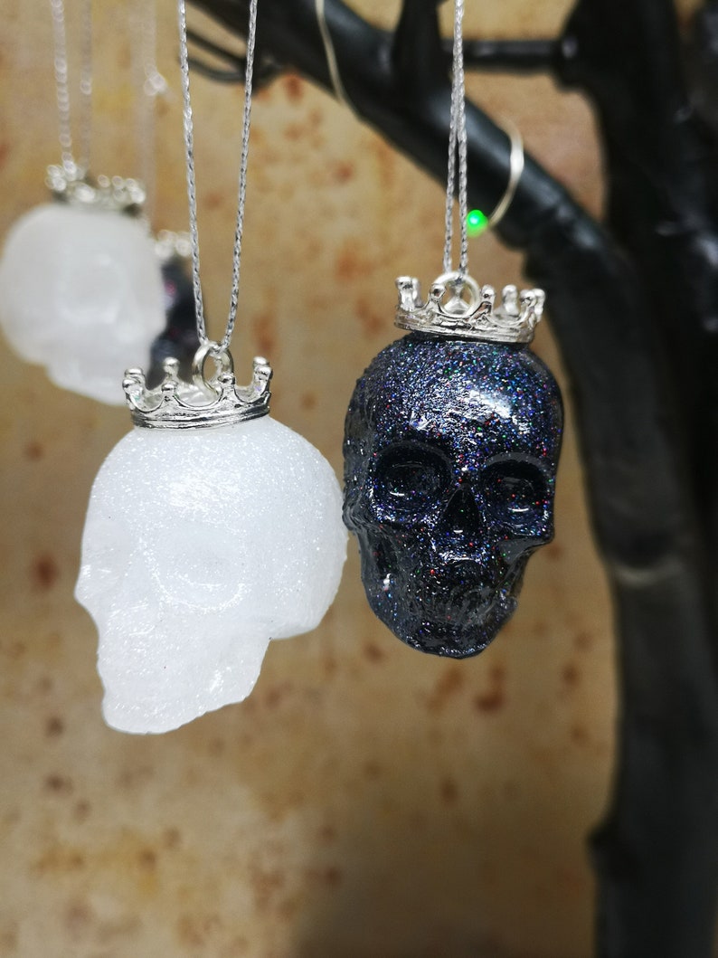 May include: Two glittery skull ornaments with silver crowns hanging from a branch. One skull is white and the other is black.