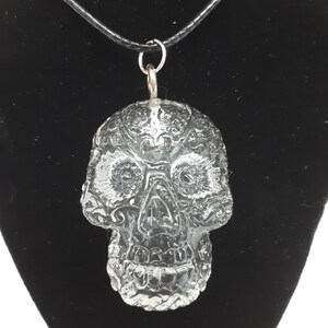 May include: A clear glass skull pendant on a black cord necklace. The skull has a detailed, intricate design.