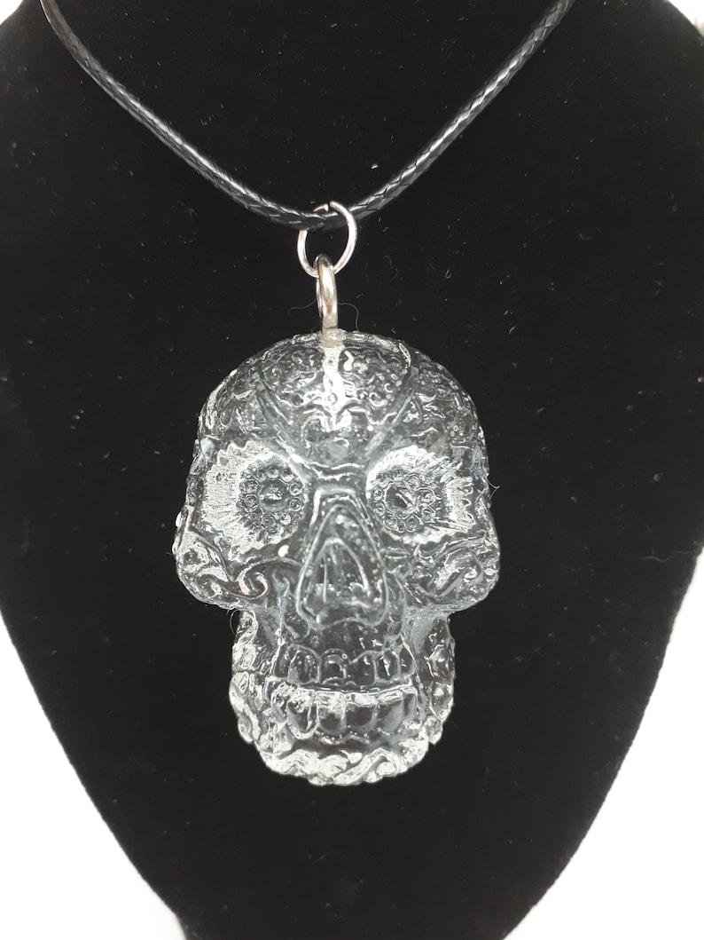 May include: A clear glass skull pendant on a black cord necklace. The skull has a detailed, intricate design.