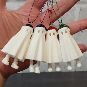 May include: Five white ghost ornaments with different coloured hats. The hats are purple, red, green, and black. The ghosts are hanging from strings.