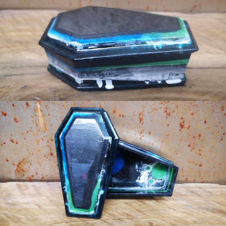 May include: A black and blue coffin-shaped box with a green and white interior. The box is decorated with a blue and green swirl pattern.