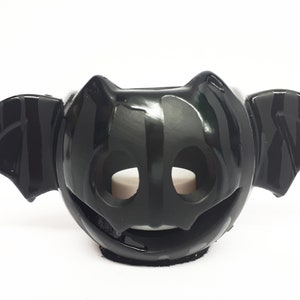 May include: Black ceramic bat candle holder with a textured surface and a cut-out design. The holder has two wings and a face with two holes for a tea light candle.