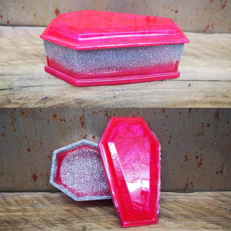 May include: A pink and silver coffin-shaped trinket box with a glitter finish. The box is open and the inside is visible.
