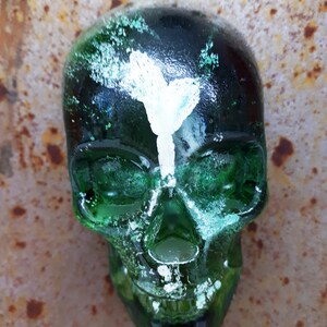 May include: A green glass skull with white paint accents. The skull has a detailed design and a textured surface.