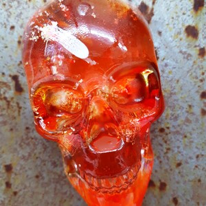 May include: A red glass skull with white and gold accents. The skull is translucent and has a detailed design.