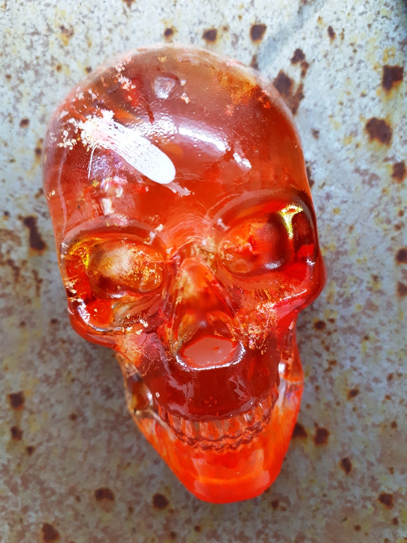 May include: A red glass skull with white and gold accents. The skull is translucent and has a detailed design.