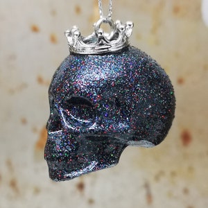 May include: A black glitter skull pendant with a silver crown on top. The skull is a dark black with iridescent glitter embedded in the resin.