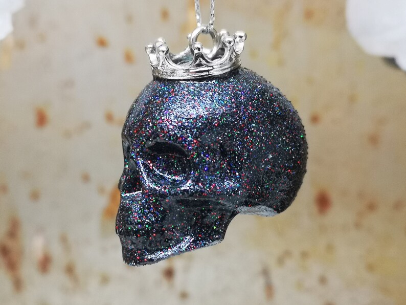 May include: A black glitter skull pendant with a silver crown on top. The skull is a dark black with iridescent glitter embedded in the resin.
