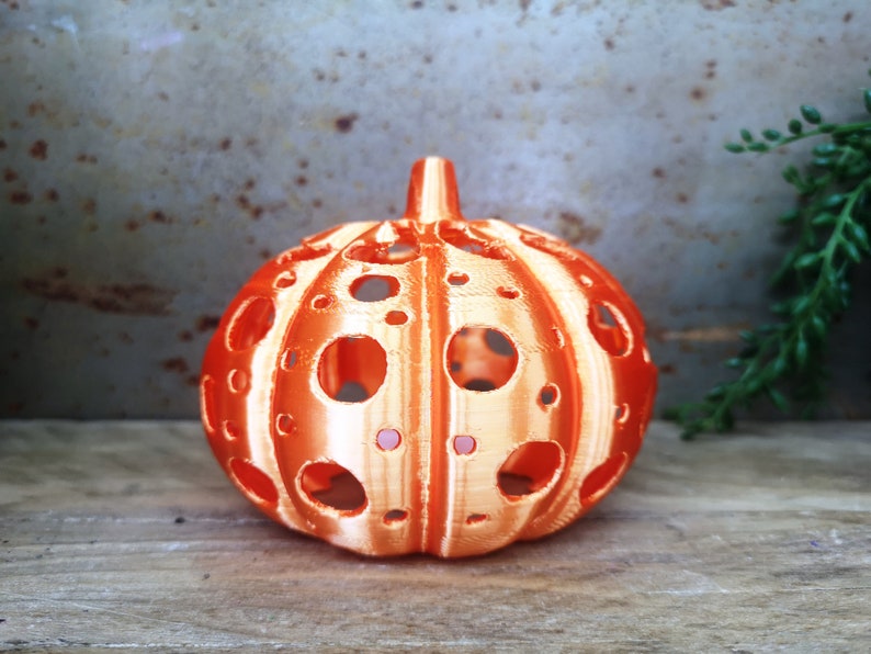 May include: Orange and white pumpkin-shaped candle holder with a decorative, patterned design and multiple cut-out holes.