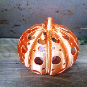 May include: An orange pumpkin-shaped candle holder with a decorative, openwork design. The candle holder is made of a smooth, glossy material and has a slightly textured surface.