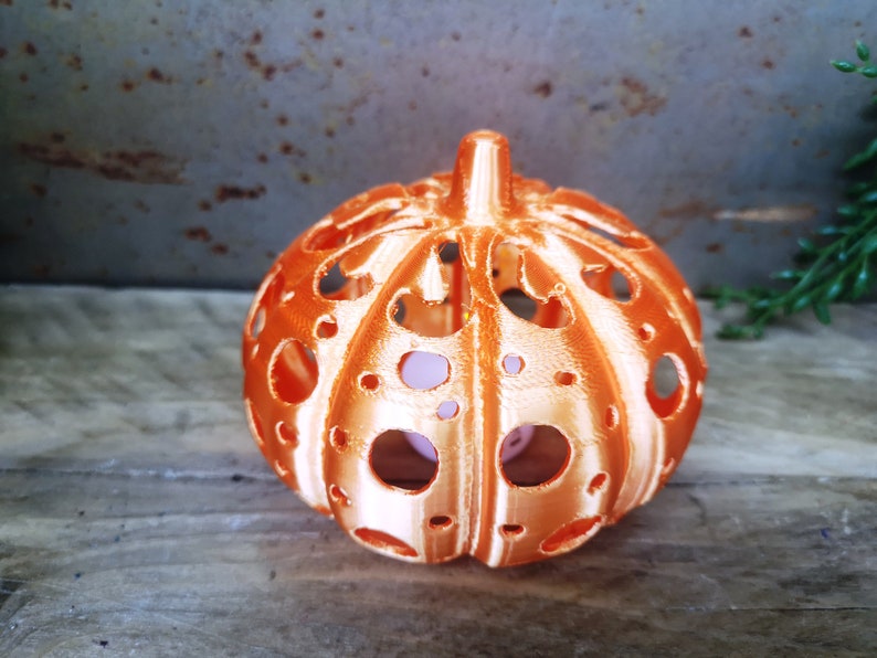 May include: An orange pumpkin-shaped candle holder with a decorative, openwork design. The candle holder is made of a smooth, glossy material and has a slightly textured surface.