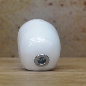 May include: White ceramic egg-shaped object with a silver threaded hole on the bottom.