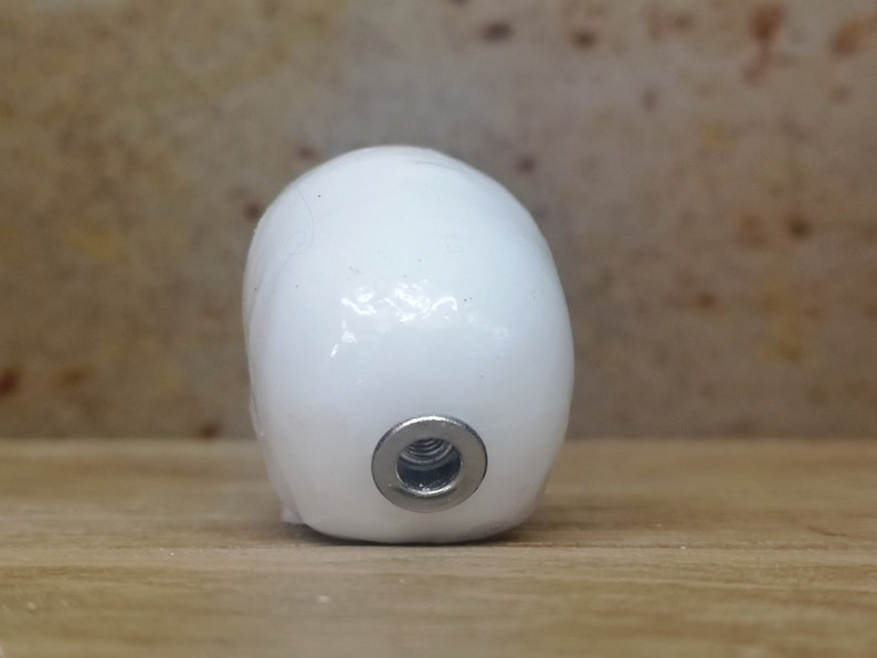 May include: White ceramic egg-shaped object with a silver threaded hole on the bottom.
