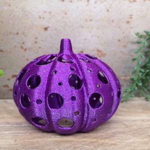 May include: A purple, 3D printed pumpkin with a hollow, dotted design. The pumpkin is made of a sparkly, textured material.